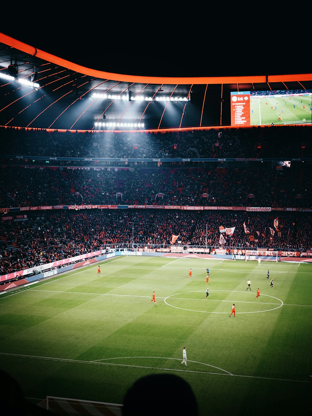 Voetballers strijden op een fel verlicht veld in een stadion tijdens een nachtwedstrijd.