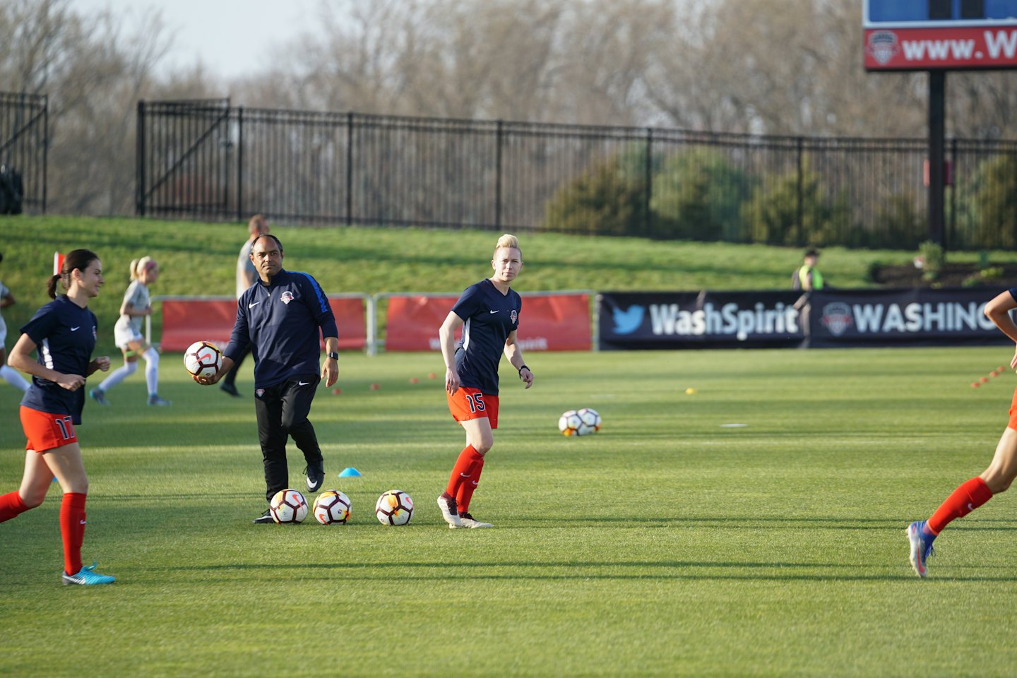 Een voetbalcoach kijkt toe hoe spelers trainen op een grasveld.